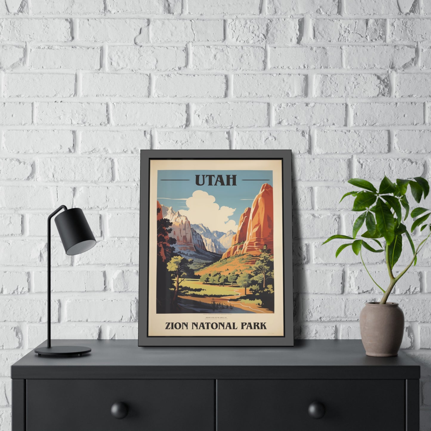 Framed vintage Utah Zion National Park travel art print on a dresser beside a plant and lamp